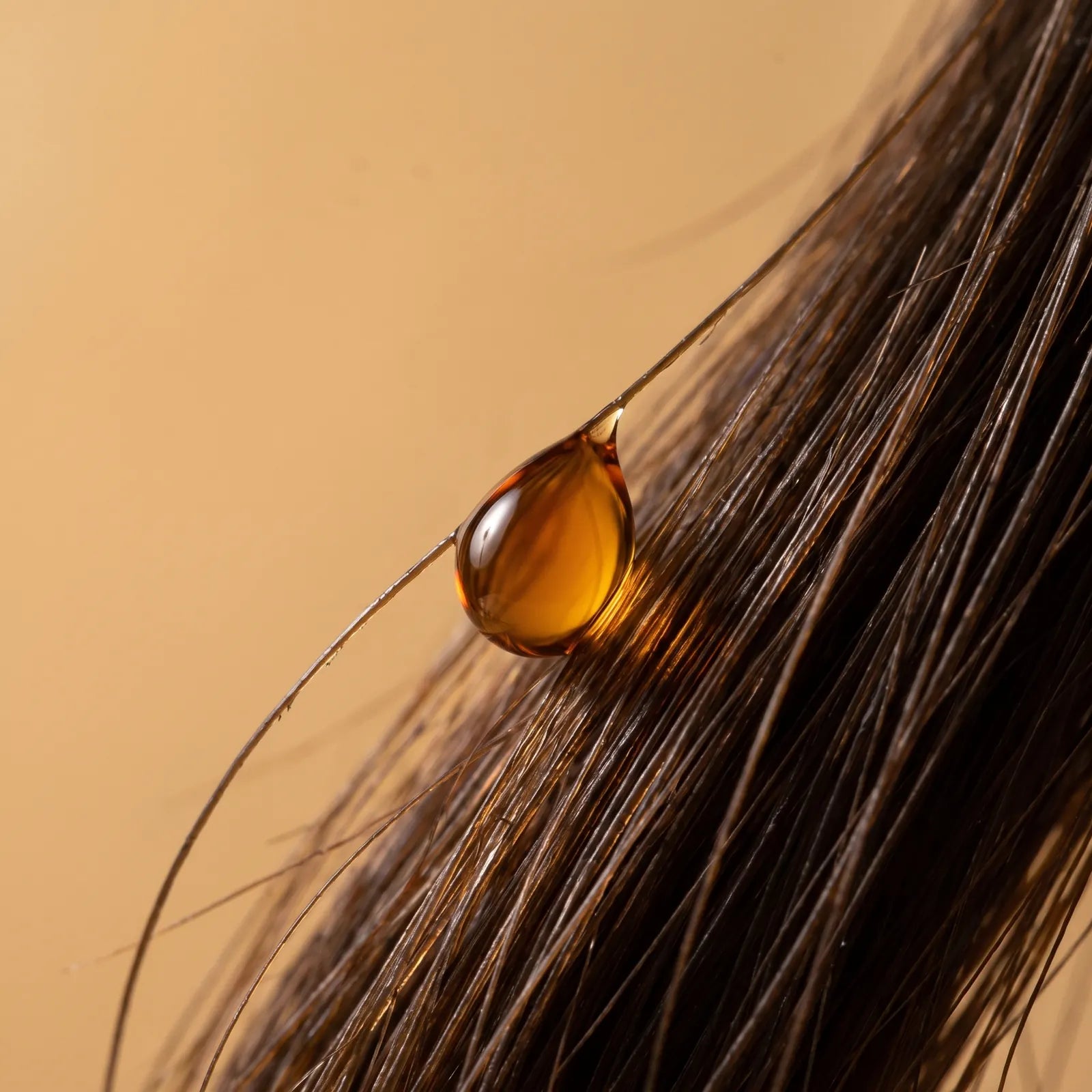 Macro di una goccia d'olio ambrato ferma su una ciocca di capelli castani