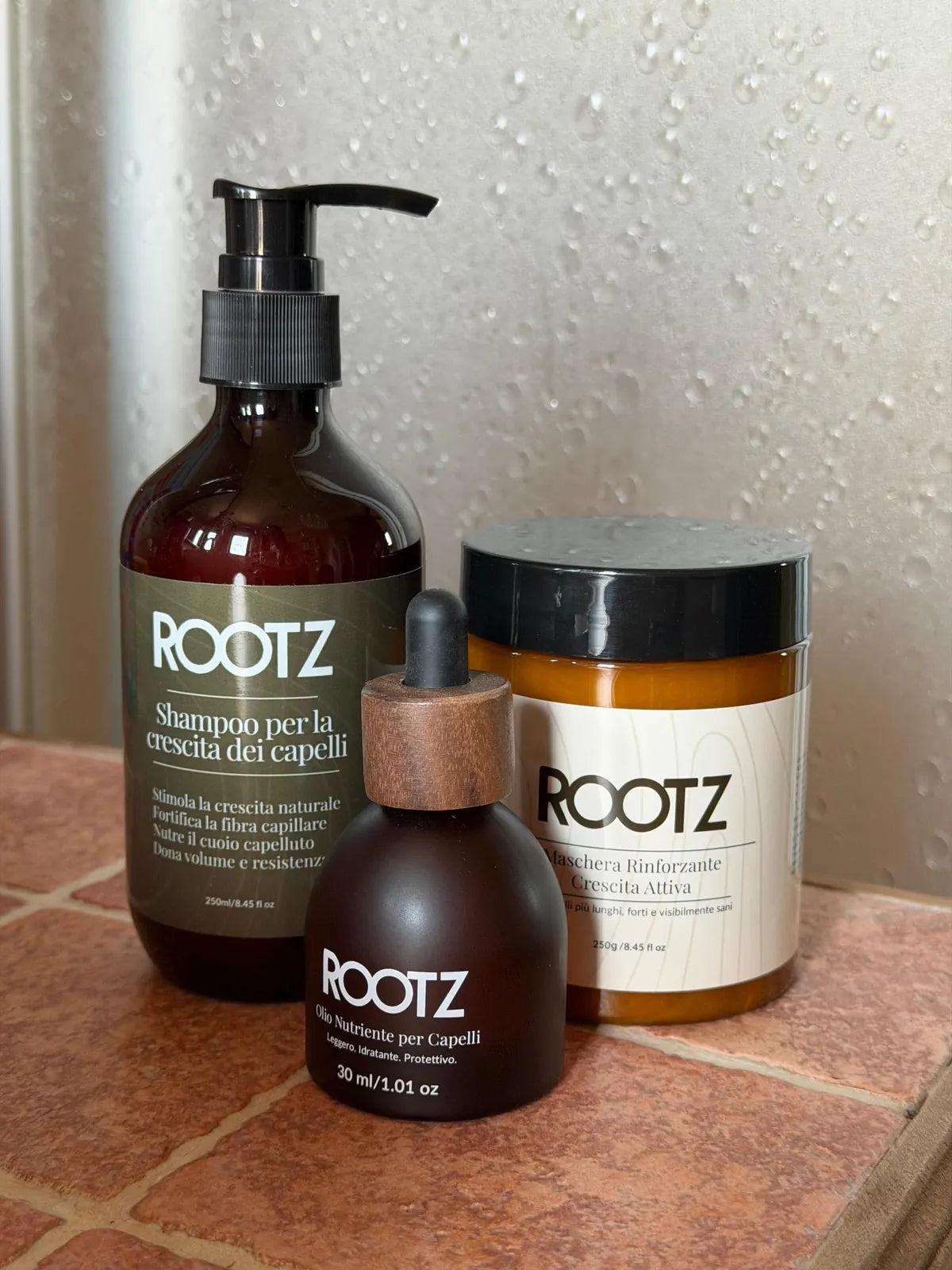 Shampoo, olio e maschera ROOTZ appoggiati sul bordo di un lavandino di casa, appena tolti dalla scatola