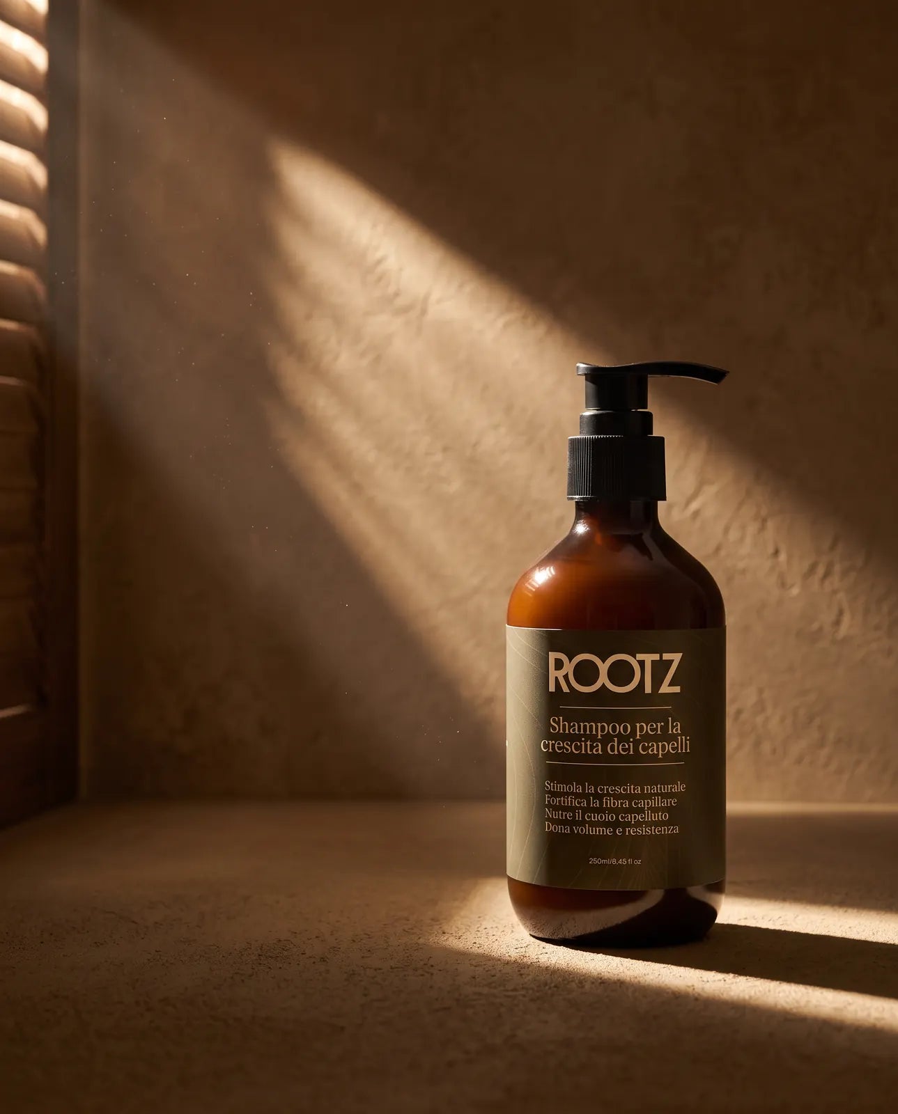 El bote de 250 ml del champú ROOTZ apoyado en el suelo en una habitación en penumbra, con la luz de una persiana en la pared