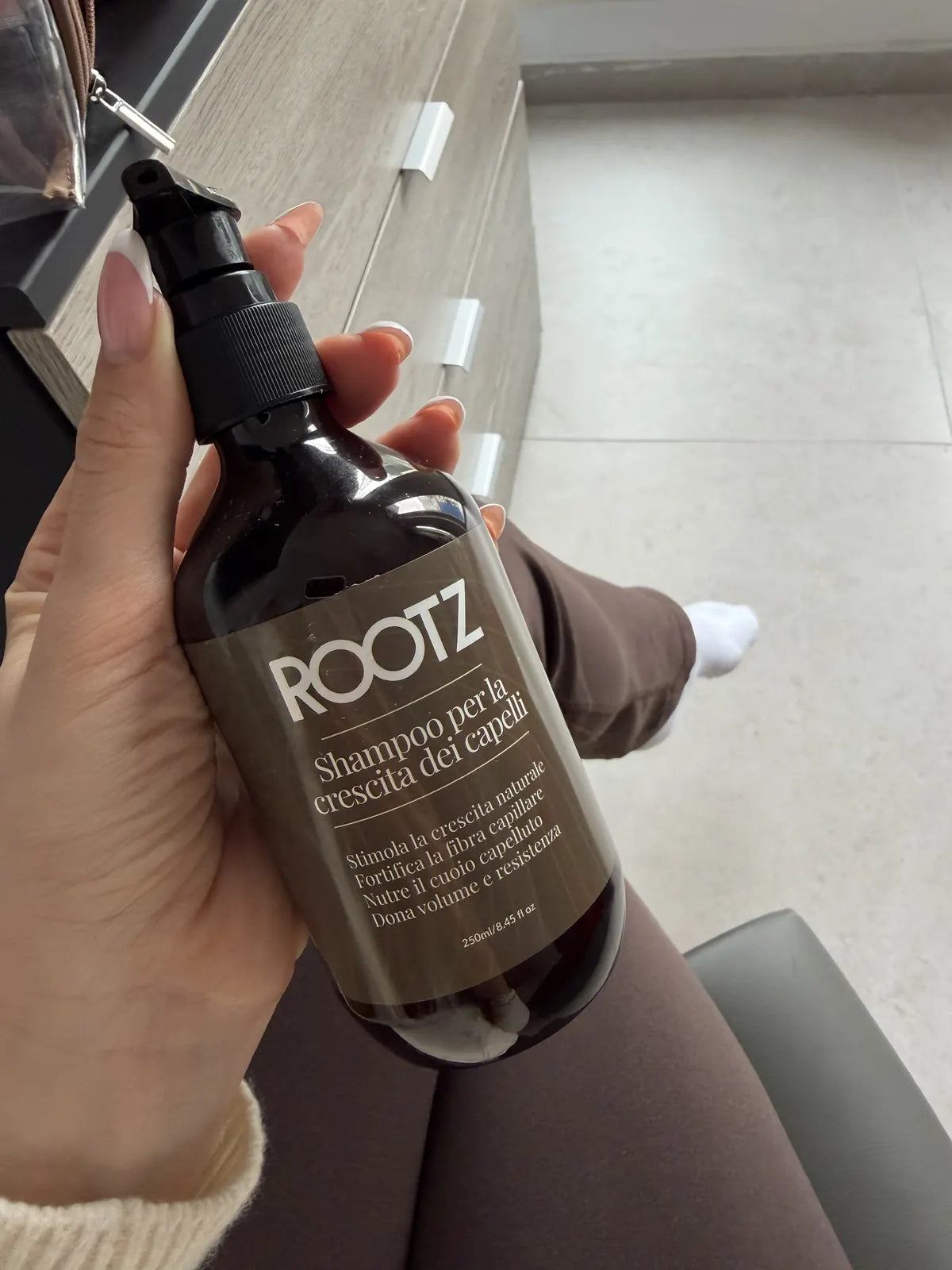 Mano di una cliente che regge il flacone di shampoo ROOTZ, seduta in casa